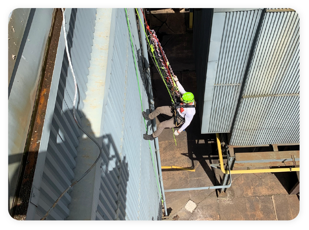 Worker using rope access equipment while scaling the exterior of an industrial structure.